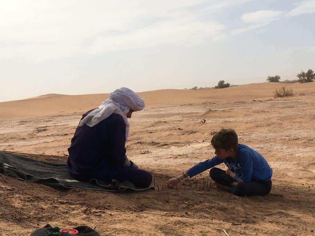 Un guide nomade joue avec un enfant lors d'un trek familial dans le sahara marocain.